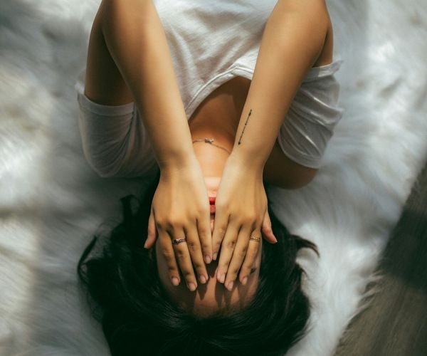 young woman lays in bed with her hands in her head as she struggles with mental health issues