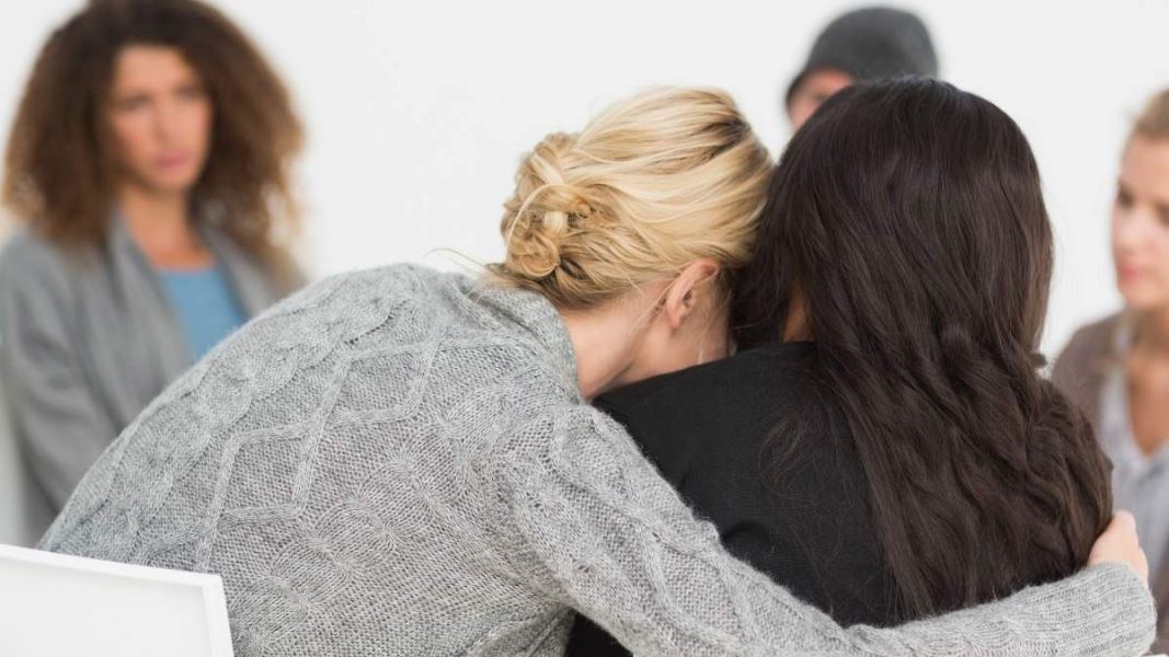 two woman embrace sitting next to each other as they support one another through mental health struggles