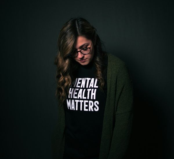 young woman standing alone in a dark room with a shirt that reads "Mental health matters".