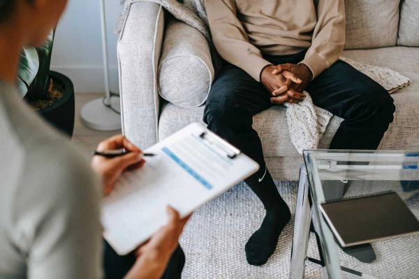 a man sits in a therapy session with a therapist who is treating him for mental health issues