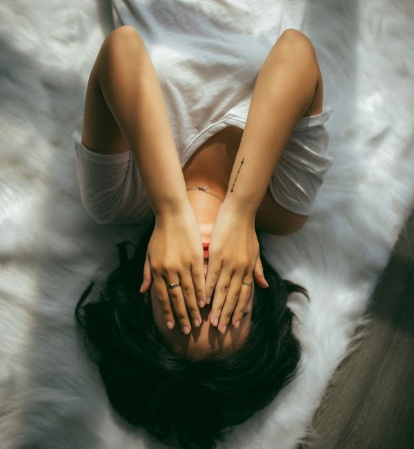 young woman lays in bed with her hands in her head as she struggles with mental health issues