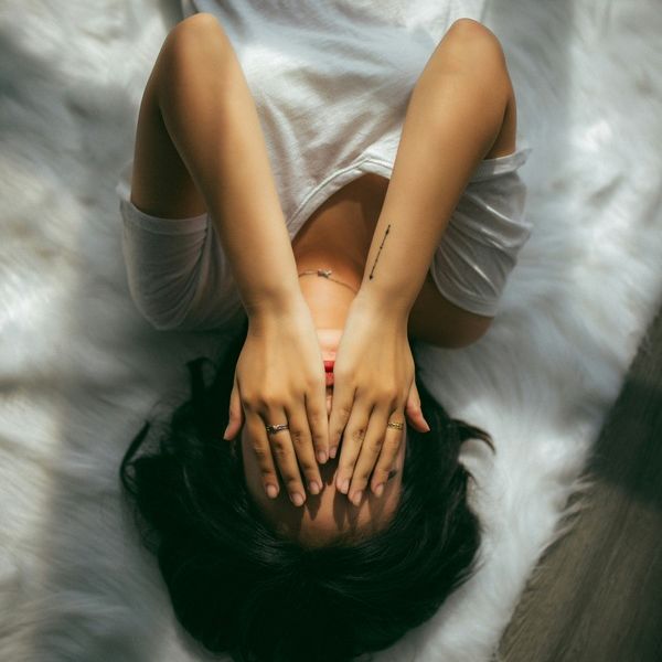 young woman lays in bed with her hands in her head as she struggles with mental health issues