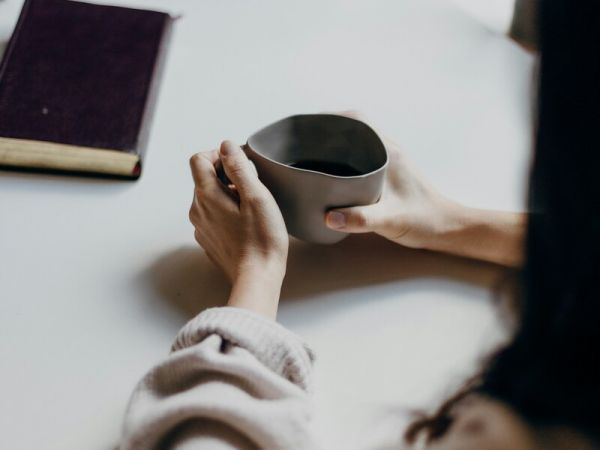 a woman sits across from her friend drinking coffee as they discuss mental health