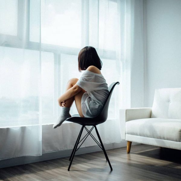 young girl sits in a chair alone by a window as she struggles with mental health issues