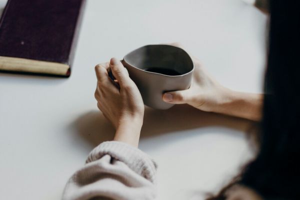 a woman sits across from her friend drinking coffee as they discuss mental health