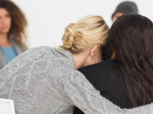 two woman embrace sitting next to each other as they support one another through mental health struggles