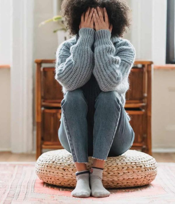 young girl sits on the floor with her head in her hands as she struggles with mental health