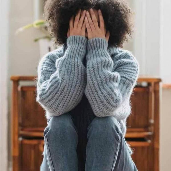young girl sits with her hands in her head as she struggles with mental health issues