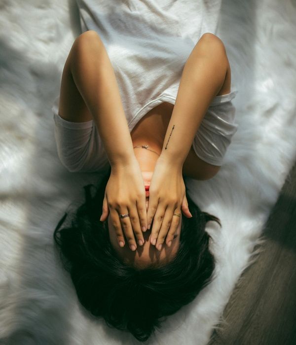 young woman lays in bed with her hands in her head as she struggles with mental health issues