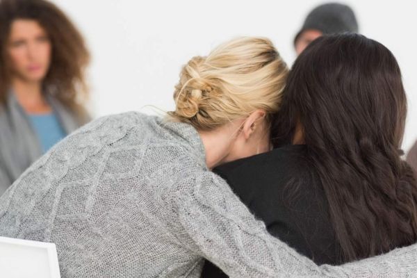 two woman embrace sitting next to each other as they support one another through mental health struggles