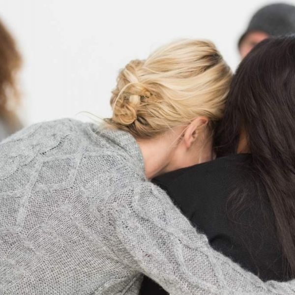 two woman embrace sitting next to each other as they support one another through mental health struggles