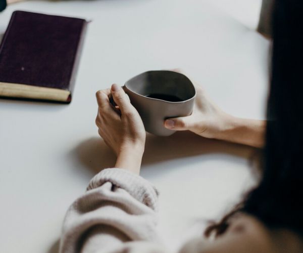 a woman sits across from her friend drinking coffee as they discuss mental health