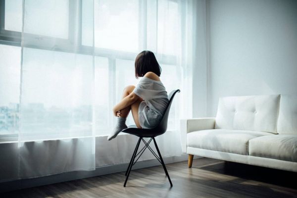 young girl sits in a chair alone by a window as she struggles with mental health issues